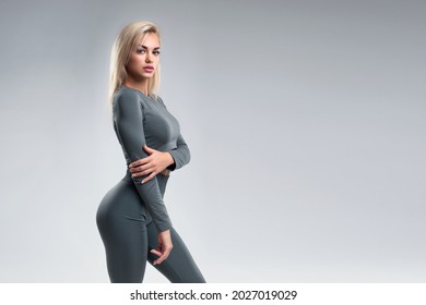 Stylish portrait of a beautiful girl in sportswear with clean skin. A model with a sporty figure in leggings and a top. Studio portrait of a young girl with a perfect body on a gray background.