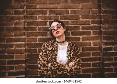 Stylish Portrait Of Young Serious Model With Crossed Arms Wearing Trendy Leopartd Print Faux Fur Coat, Fashion Sunglasses, Posing On Red Brick Wall Texture Grunge Background