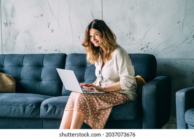 Stylish Pregnant Business Woman Dressed Casually Sitting In Sofa Working With Laptop In Modern Hall Or Office Interior. Pregnancy, Maternity Leave Concept.