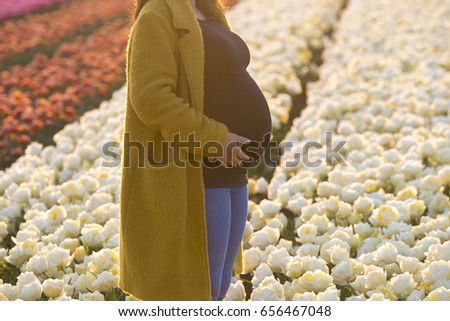 A stylish pregnant lady standing in a field of magnificent flowers.