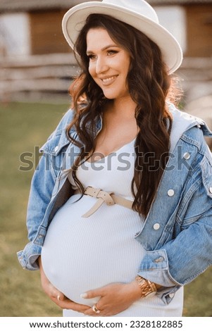 Stylish pregnant woman in a white hat in the countryside.