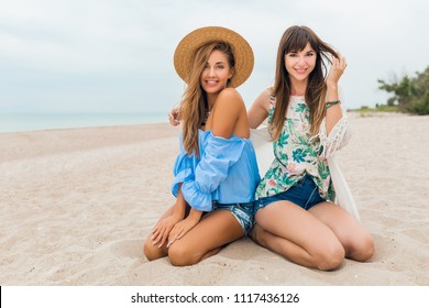 stylish pretty women on summer vacation on tropical beach, bohemian style, friends travel together, fashion trend, accessories, smiling, happy emotion, positive mood, straw hat, sitting on sand - Powered by Shutterstock