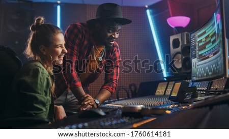 Stylish Producer and Audio Engineer Working together in Music Recording Studio on New Album, Talk, Use Control Desk Equalizer, Mixing Board and Software to Create Hit Song. Artist and Musician Collab