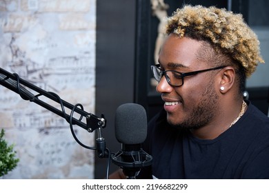 Stylish Professional Presenter Smiles During A Live Broadcast, Conducts A Fascinating Conversation With The Audience. A Young And Handsome Black DJ With Glasses Plays Music In His Home Studio. 