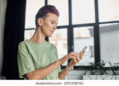 stylish queer manager in casual attire looking at smartphone while standing in modern office - Powered by Shutterstock