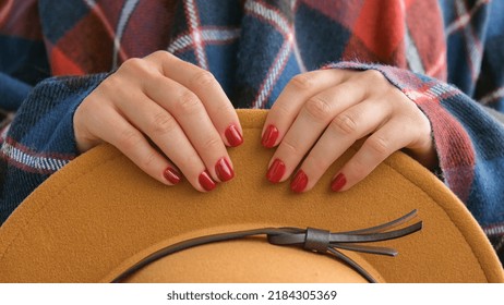 Stylish red female nails. Woman in poncho holding brown trendy hat. Modern Beautiful manicure. Autumn winter nail design concept of beauty treatment. Gel nails. Skin care. Wellness. Trendy colors. - Powered by Shutterstock