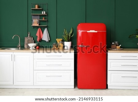 Stylish refrigerator and counters near green wall in kitchen