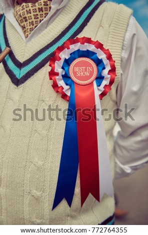 A stylish retro vintage fashionable gentleman, wearing a cricket jumper and a best in show rosette award badge,  in a Best dressed award at a vintage event.
