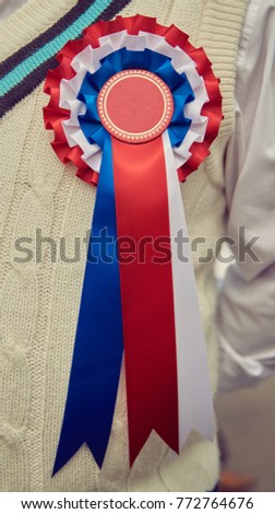 A stylish retro vintage fashionable gentleman, wearing a cricket jumper and a best in show rosette award badge,  in a Best dressed award at a vintage event.