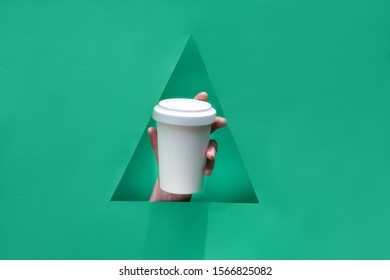 Stylish Reusable Eco Coffee Travel Mug, Bamboo Cup With Lid In Hand Through Triangular Paper Hole In Shape Of Christmas Tree. Green Paper Background, Keep Cup Mockup With Copy Space.