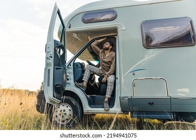 Stylish rich young bearded man sitting on the driver seat of his own modern camper van with open doors in a rural area. . High quality photo - Powered by Shutterstock