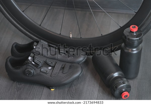 stylish road bike shoes, cycling water\
bottles and a carbon black wheel closeup\
concept
