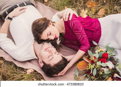 Stylish And Romantic Caucasian Couple Lie On The Grass And Leaves In The Beautiful Autumn Park. Love, Relationships, Romance, Happiness Concept.