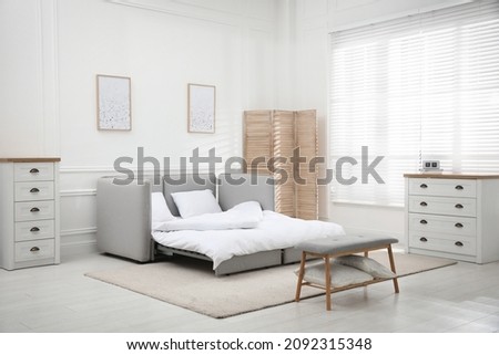 Stylish room interior with sleeper sofa near white wall. Additional place for guest