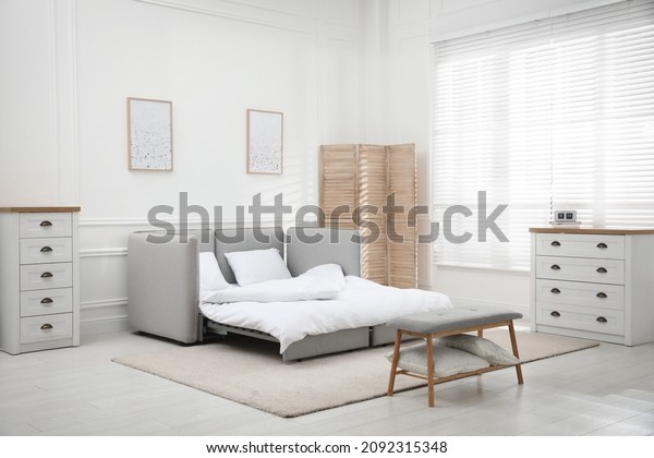 Stylish room interior with sleeper sofa near\
white wall. Additional place for\
guest