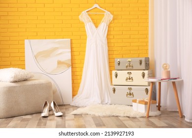 Stylish Room Interior With Storage Trunks, Ottoman And Beautiful Wedding Dress Near Yellow Brick Wall