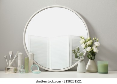 Stylish round mirror on dressing table with cosmetic products and flowers