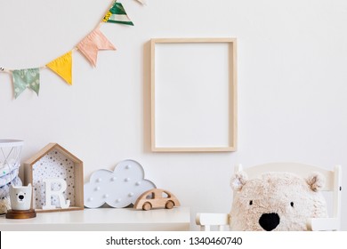 Stijlvolle scandinavische kinderkamer met mock up fotoposter frame op de witte muur. Schattig modern interieur van kinderkamer met dozen, teddybeer, speelgoed. houten accessoires en kleurrijke vlaggen. Echte foto.