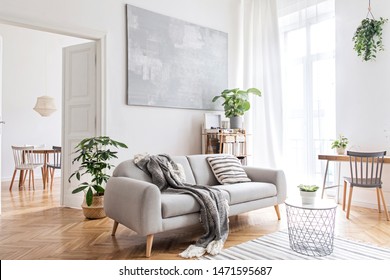 Stylish scandinavian living room with design furniture, plants, bamboo bookstand and wooden desk. Brown wooden parquet. Abstract painting on the white wall. Nice apartment. Modern decor of bright room - Shutterstock ID 1471595687