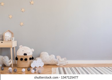 Stylish scandinavian newborn baby room with toys, children's chair, natural basket with teddy bear and small shelf. Modern interior with grey background walls, wooden parquet and stars pattern.