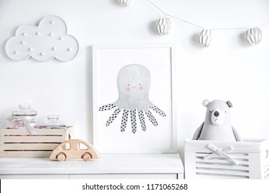 Stylish scandinavian newborn baby shelf with mock up photo frame,  box, teddy bear and toys. Modern interior with white walls and wooden accessories.