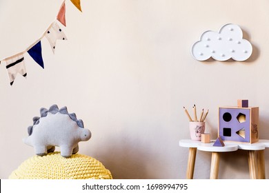 Stylish scandinavian nursery interior with plush dino, design furniture, toys, beautiful decoration and accessories in modern home decor for children room. 