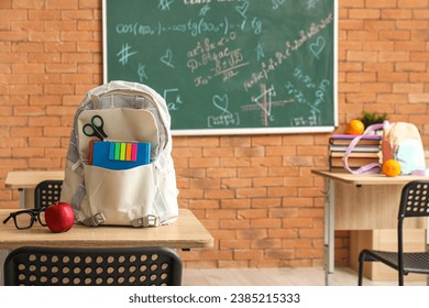 Stylish school backpack with stationery, eyeglasses and apple on desk in classroom - Powered by Shutterstock