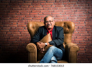 Stylish Senior Indian Man In Suit Sitting On Sofa Or Wing Chair. Portrait Of Indian Or Asian Millionaire Or Rich Man  