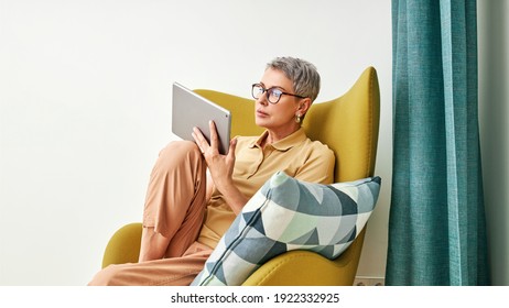 Stylish Senior Woman Relaxing At Home Reading From Digital Tablet