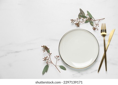 Stylish setting with cutlery and eucalyptus leaves on white marble table, flat lay. Space for text