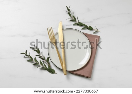 Stylish setting with cutlery and eucalyptus leaves on white marble table, flat lay
