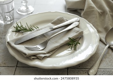 Stylish setting with cutlery, napkin, rosemary and plate on light tiled table, closeup - Powered by Shutterstock