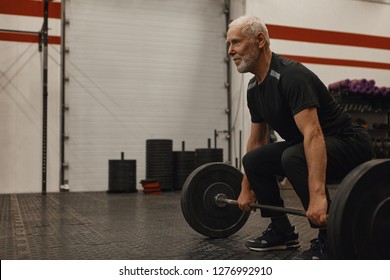 Stylish seventy year old male choosing healthy active lifestyle, training with weights indoors, lifting barbell, bulding muscular strong arms, having joufyl happy facial expression. Age and vitality - Powered by Shutterstock