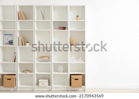 Stylish shelf unit with books and decor elements near white wall