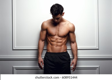 Stylish shirtless man at the white wall looking down, Horizontal studio shot. - Powered by Shutterstock