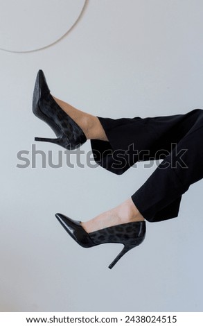 Stylish slim women feet in black high heels. Female legs in pants up in the air on white background. Elegant shoes fashion for woman. Vertical beautiful photo with lady footwear model