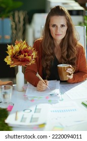 Stylish Small Business Owner Woman With Autumn Yellow Leaves And Cup Of Coffee In The Modern Green Office.