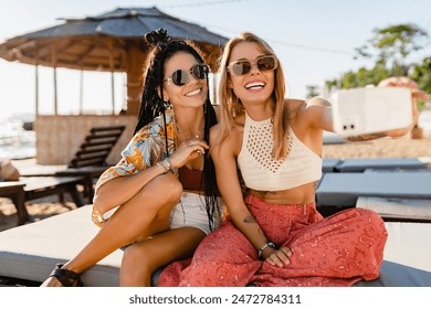 stylish smiling beautiful women relaxing having fun on beach in summer fashion trend outfit, colorful apparel boho style, tropical vacation wearing sunglasses, using smartphone taking selfie picture - Powered by Shutterstock