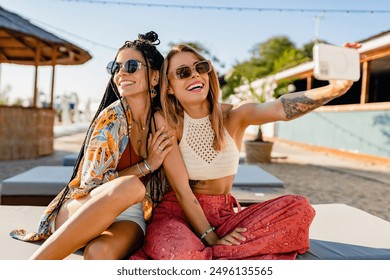 stylish smiling beautiful women relaxing having fun on beach in summer fashion trend outfit, colorful apparel boho style, tropical vacation wearing sunglasses, using smartphone taking selfie picture - Powered by Shutterstock