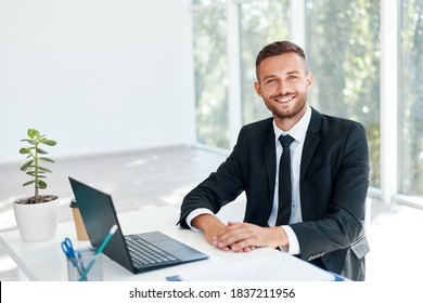 Stylish smiling businessman in elegant suit sitting at his desk in a bright modern office. business success concept - Powered by Shutterstock