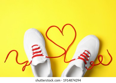 Stylish sneakers and red shoe laces in shape of heart on yellow background, flat lay - Powered by Shutterstock