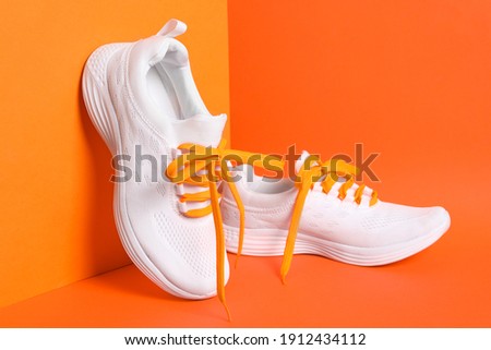 Stylish sneakers with shoe laces on orange background