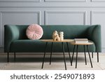 Stylish sofa with cushion, books and decor elements on nesting tables in room