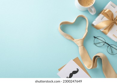 Stylish and sophisticated Father's Day idea. Overhead shot of heart shaped necktie, glasses, mustaches, present box, greeting card, coffee mug, and blank space for advert on pastel blue background