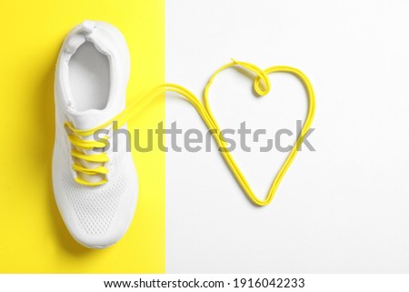 Stylish sportive shoe and yellow laces in shape of heart on color background, flat lay