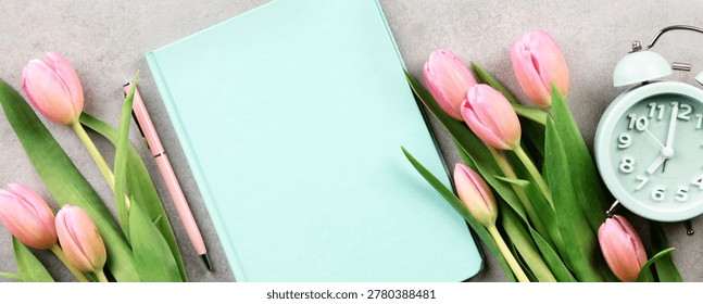 Stylish spring flat lay with pink tulips, pastel notebook, pen, eyeglasses, and alarm clock on a neutral background. Fresh seasonal workspace concept with copy space for planning or lifestyle themes.
