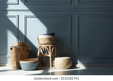 Stylish stool and many wicker baskets near light grey wall indoors