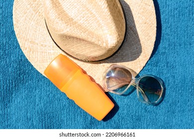 Stylish Straw Hat, Bottle Of Sunblock And Sunglasses On Soft Blue Beach Towel, Flat Lay