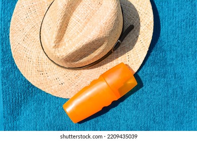 Stylish Straw Hat And Bottle Of Sunblock On Soft Blue Beach Towel, Flat Lay