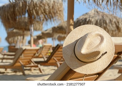 Stylish straw hat on wooden sunbed at beach, space for text